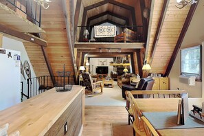A spacious loft-style living area with high ceilings, wooden beams, a dining table, and a cozy seating arrangement. - Cooper's Landing by Taylor Made Deep Creek (Swanton)