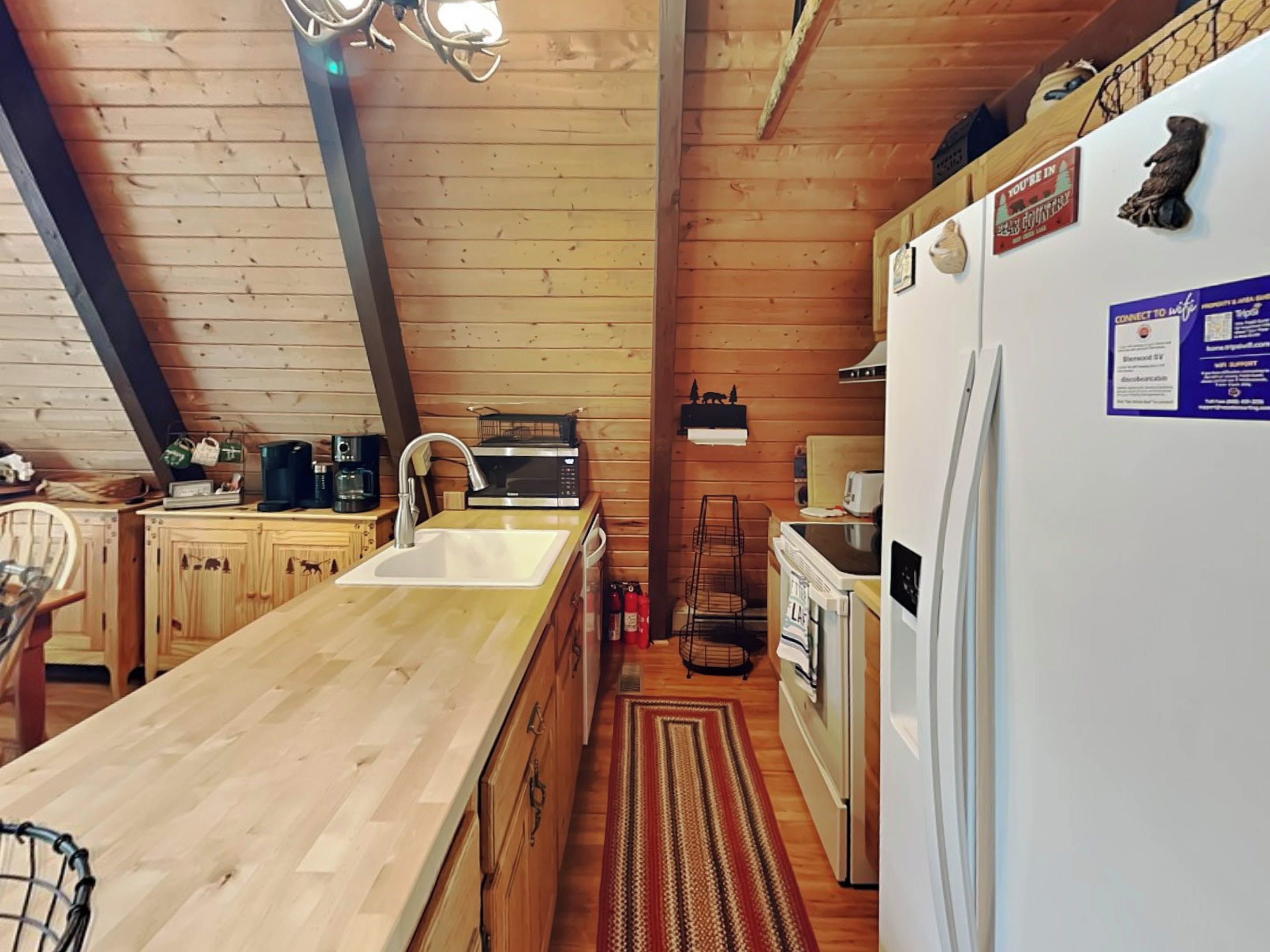A kitchen with wooden cabinets, a sink, a microwave, a refrigerator, and a coffee maker.