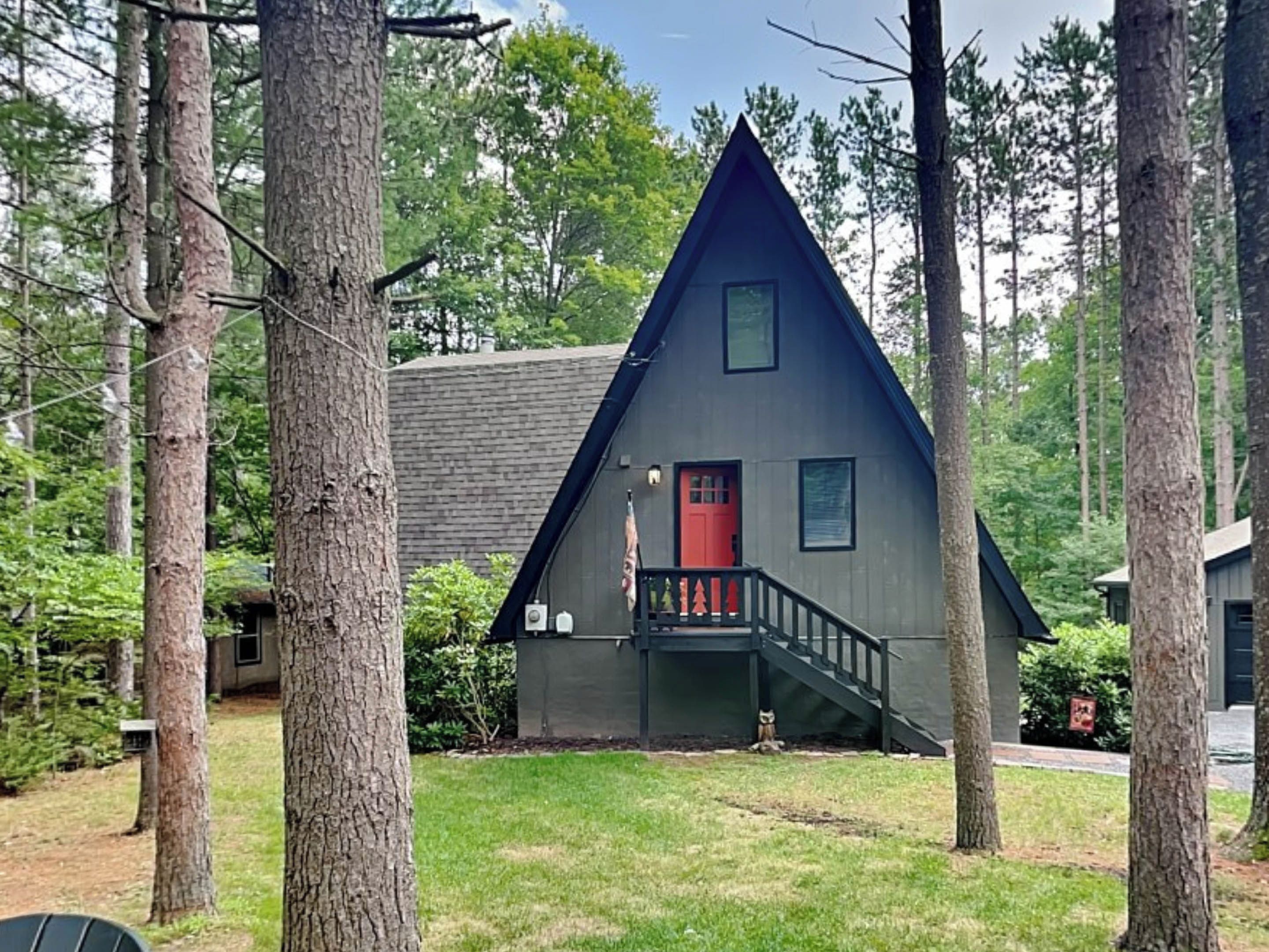 A cabin with a steeply pitched roof, a red door, and a small porch with a staircase.