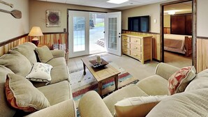 A living room with a sofa, coffee table, and a television. There is a door leading to a bedroom with a bed. - Cooper's Landing by Taylor Made Deep Creek (Swanton)