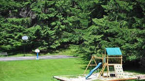 A playground with a swing set and slide, surrounded by a grassy area and dense trees. - Cooper's Landing by Taylor Made Deep Creek (Swanton)