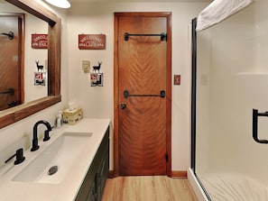 A bathroom with a wooden door, a sink with a mirror, and a towel rack. - Cooper's Landing by Taylor Made Deep Creek (Swanton)