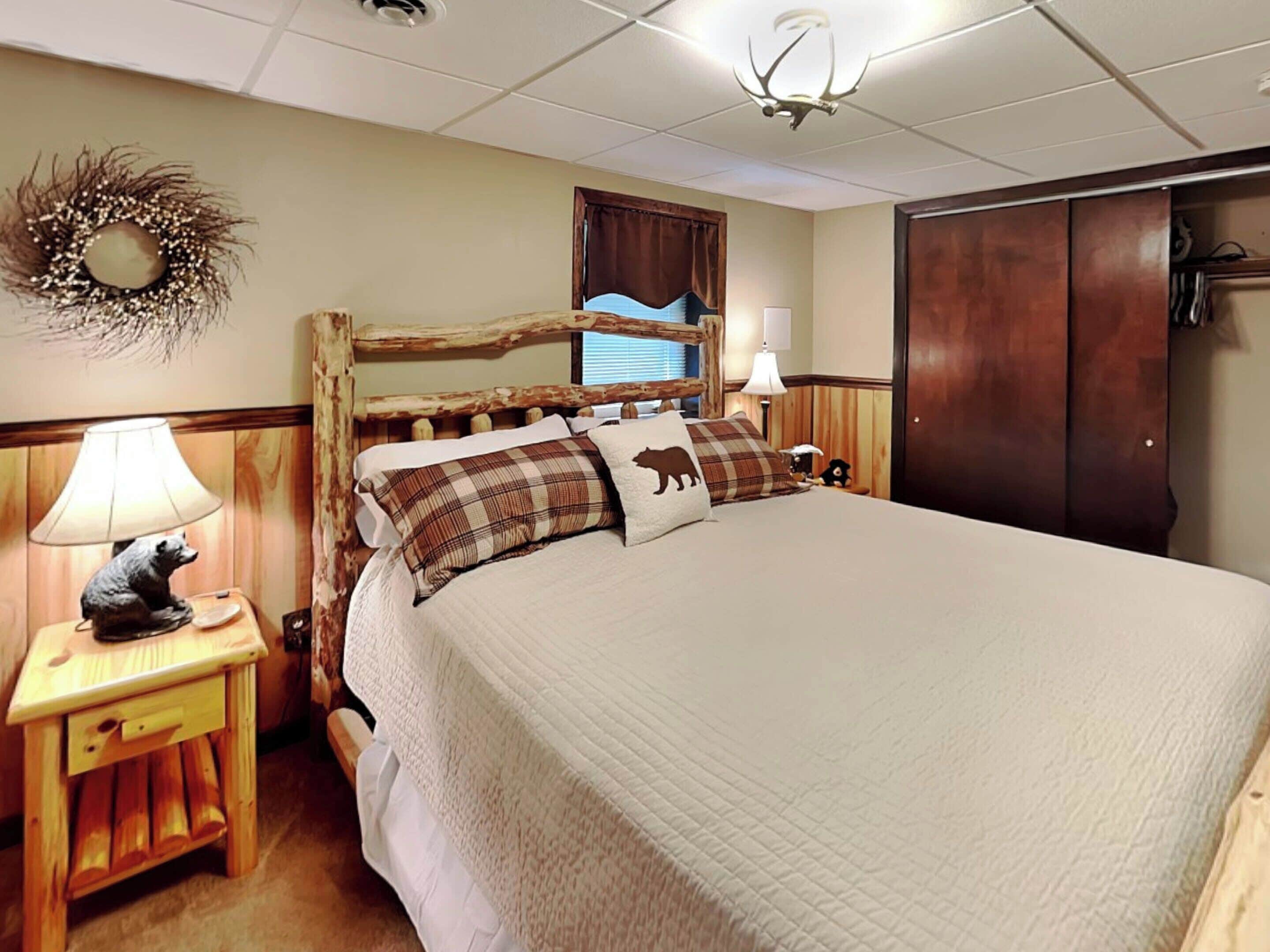 A bedroom with a large bed, a wooden headboard, a nightstand with a lamp, and a wall-mounted light fixture.