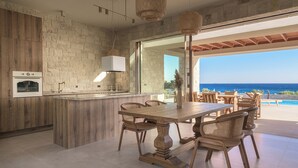 A modern kitchen with a stone backsplash, a built-in oven, and a large dining area with a view of the ocean.
