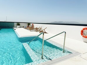 Une piscine sur le toit, avec une eau d’un bleu limpide, entourée de chaises longues et d’une bouée de sauvetage.