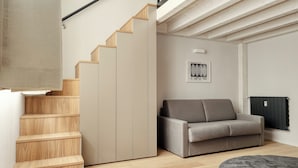 Una sala de estar moderna con un sofá, un tapete gris y una escalera con escalones de madera.