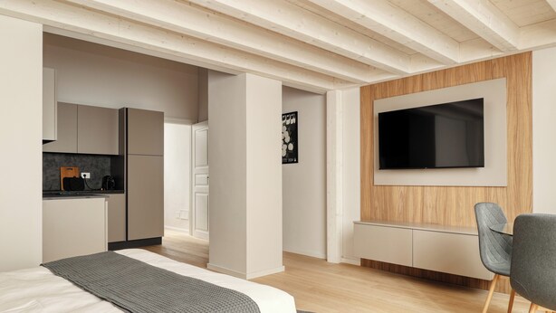 Un dormitorio moderno con cama, televisor montado en la pared y una cocina al fondo.