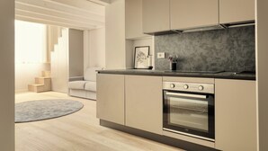 Una cocina moderna con horno empotrado, encimera gris y una escalera que lleva a una sala de estar.