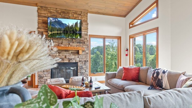 Ein gemütliches Wohnzimmer mit Kamin aus Naturstein, einem großen Fenster mit schöner Aussicht und einer komfortablen Sitzecke.