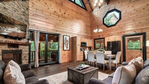 Un vaste espace de vie doté d’une cheminée, de murs en bois et d’un coin repas offrant une vue sur l’extérieur.