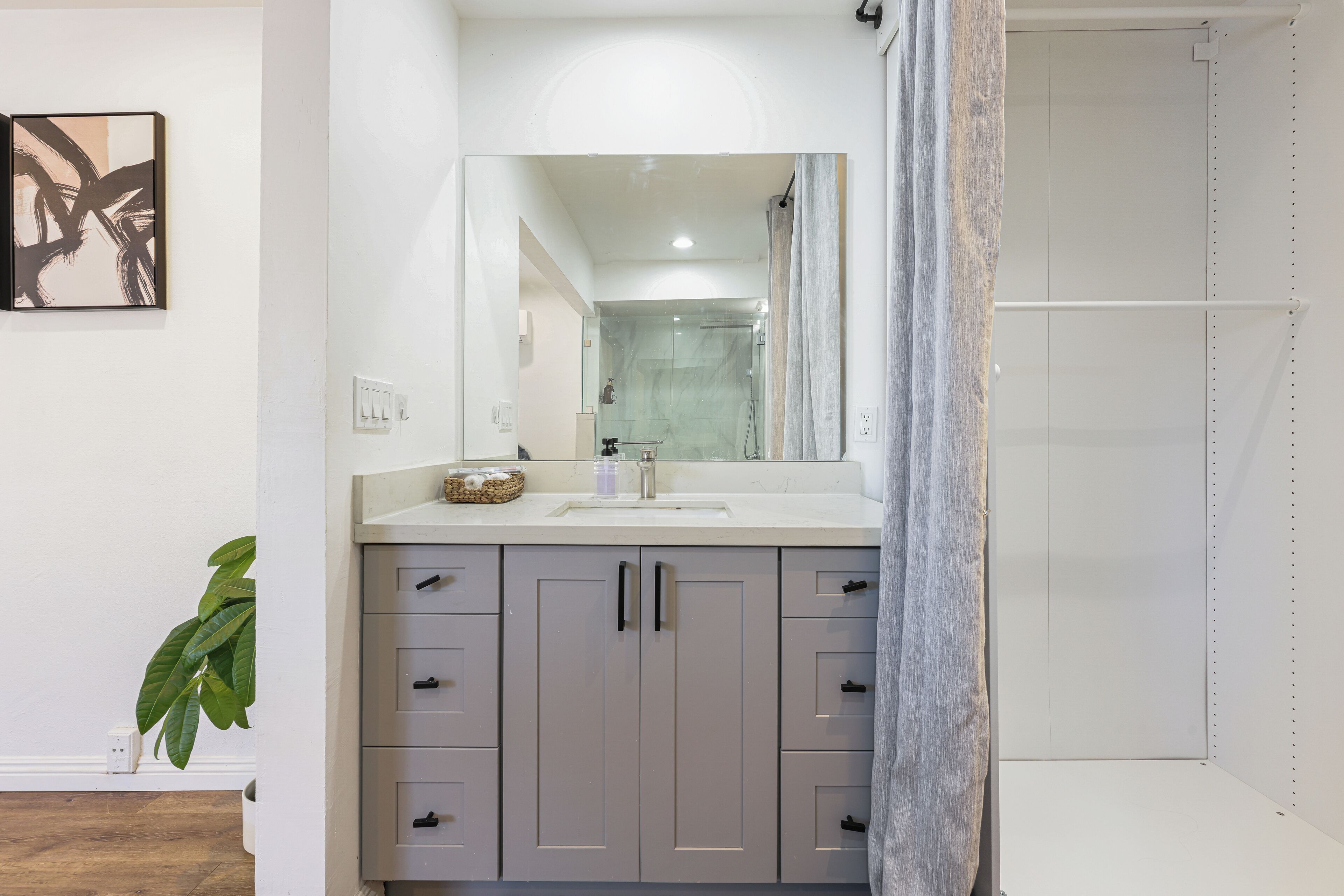 Een moderne badkamer met een grote spiegel, grijze kastjes en een douchehoek.