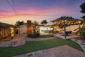 Un jardin avec une pergola, un espace salon extérieur et un chemin pavé en briques.
