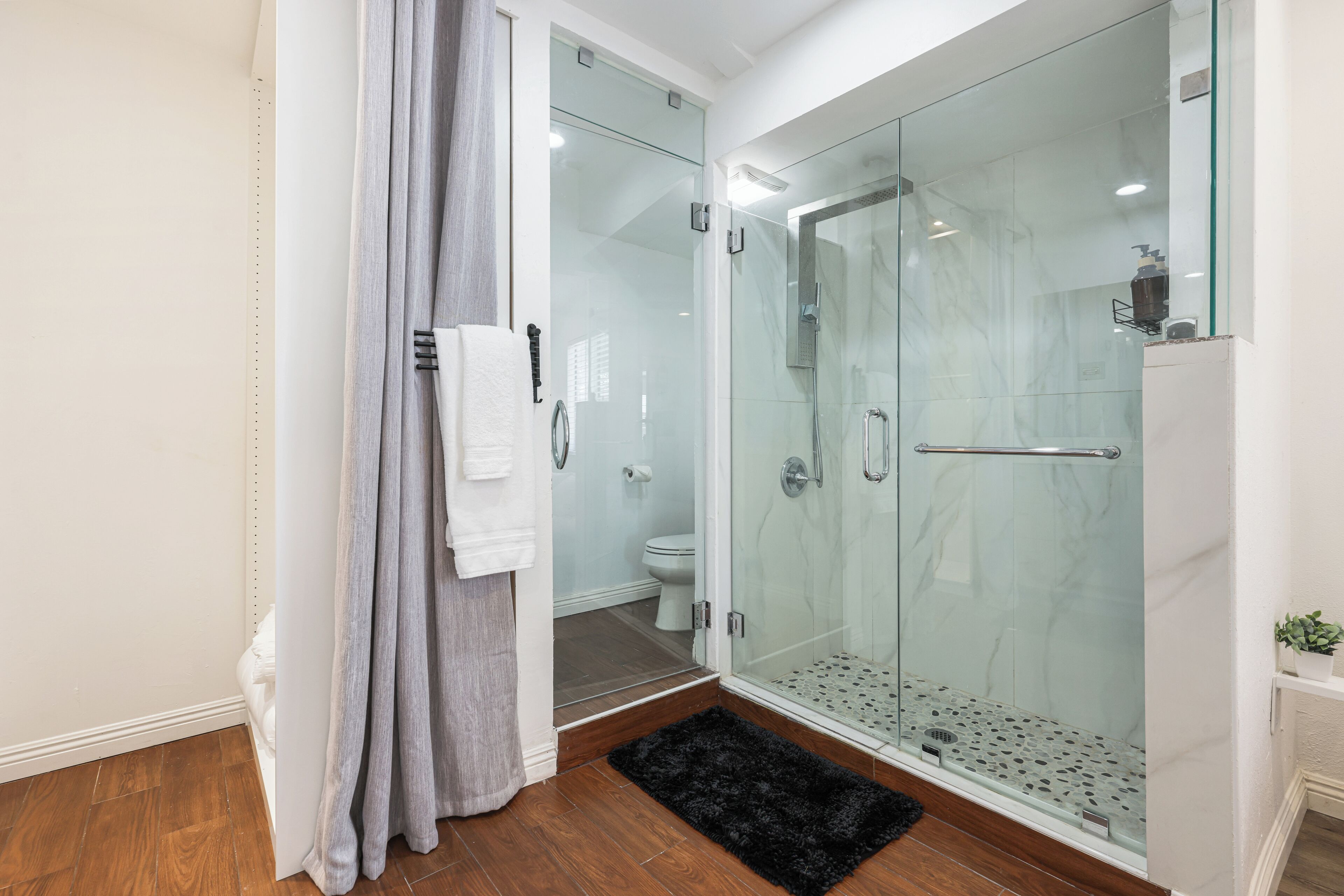 Une salle de bain moderne avec une douche à parois de verre, des toilettes et un tapis noir sur le sol.