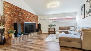 Ein Wohnzimmer mit Backsteinwand, Holzboden, einem Flachbildfernseher, einer Couch und einem Couchtisch.