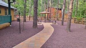 A wooden deck with a pathway leading to a seating area with tables and chairs, surrounded by trees. - Roomy Cabin in TALL Pines w/ Fenced Yd, A/C,  4  Bd/2 Ba, 75" TV + 593 movies (Pinetop)
