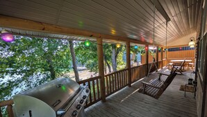 Una terraza cubierta al aire libre con una parrilla, bancos de madera y luces colgantes.