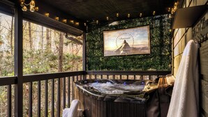 A hot tub with a wooden deck, a framed picture of a mountain, and a towel rack. - Romantic cabin with Sauna, fitness room in Gatlinburg, near NP, Pet-Friendly (Gatlinburg)
