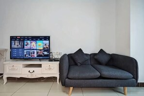 A living room with a flat-screen TV on a white TV stand, a dark grey sofa, and a white cabinet with drawers.