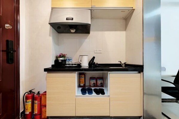 A compact kitchen with a black countertop, a white wall, and a wooden cabinet below. - Aiqinghai apartment (Guangzhou)