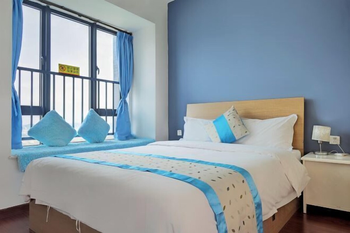 A hotel room with a bed, a window with curtains, a nightstand, and a lamp.
