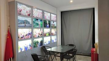 A room with a dining table, chairs, a cabinet with multiple screens, and a curtain.