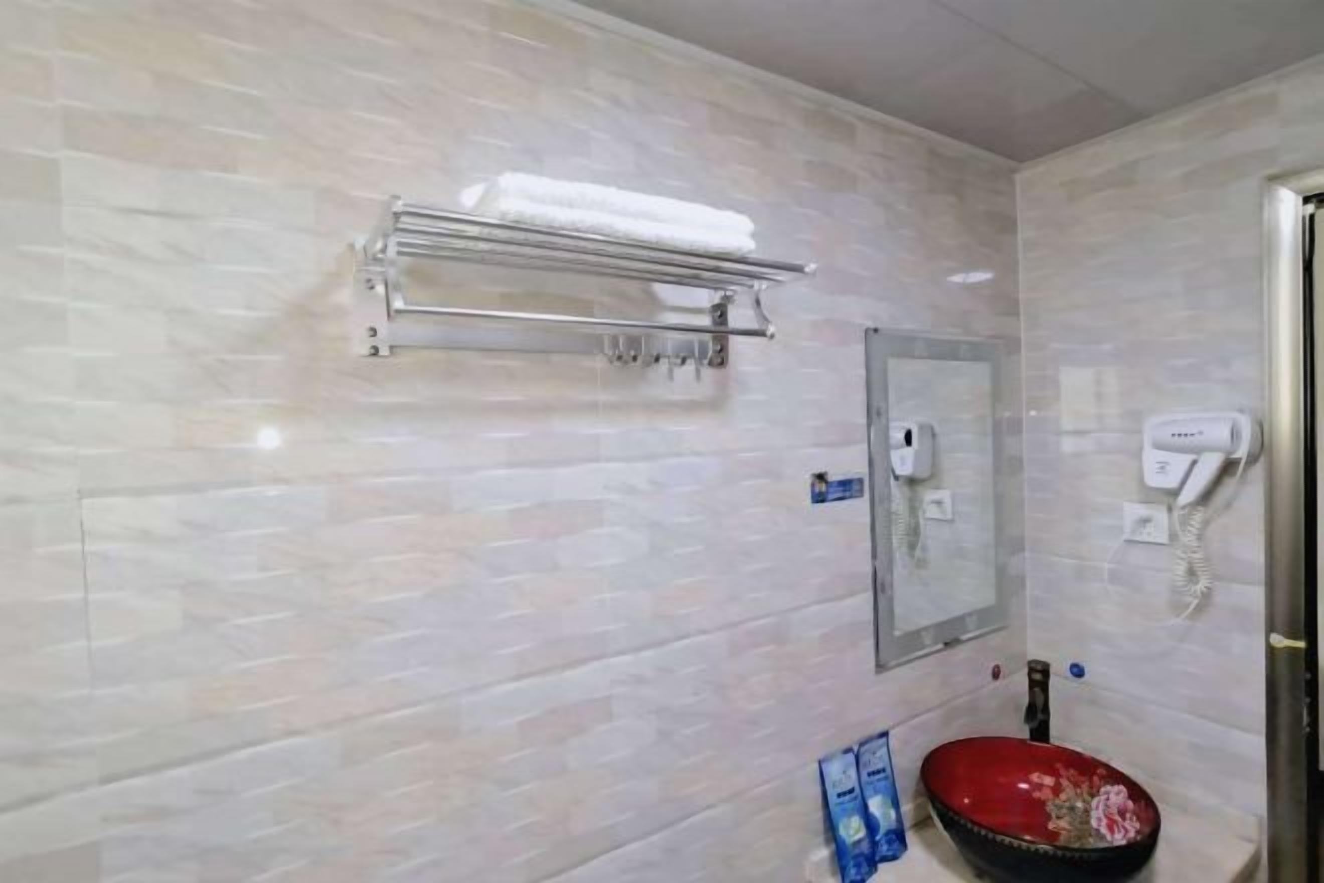 A bathroom with a tiled wall, a towel rack, a mirror, a sink with a red basin, and a telephone.