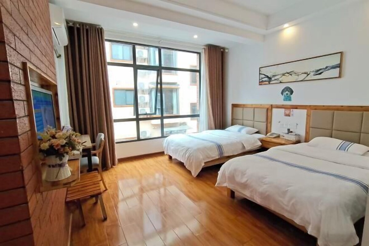 A hotel room with two beds, a desk with a chair, a window with curtains, and a painting on the wall.