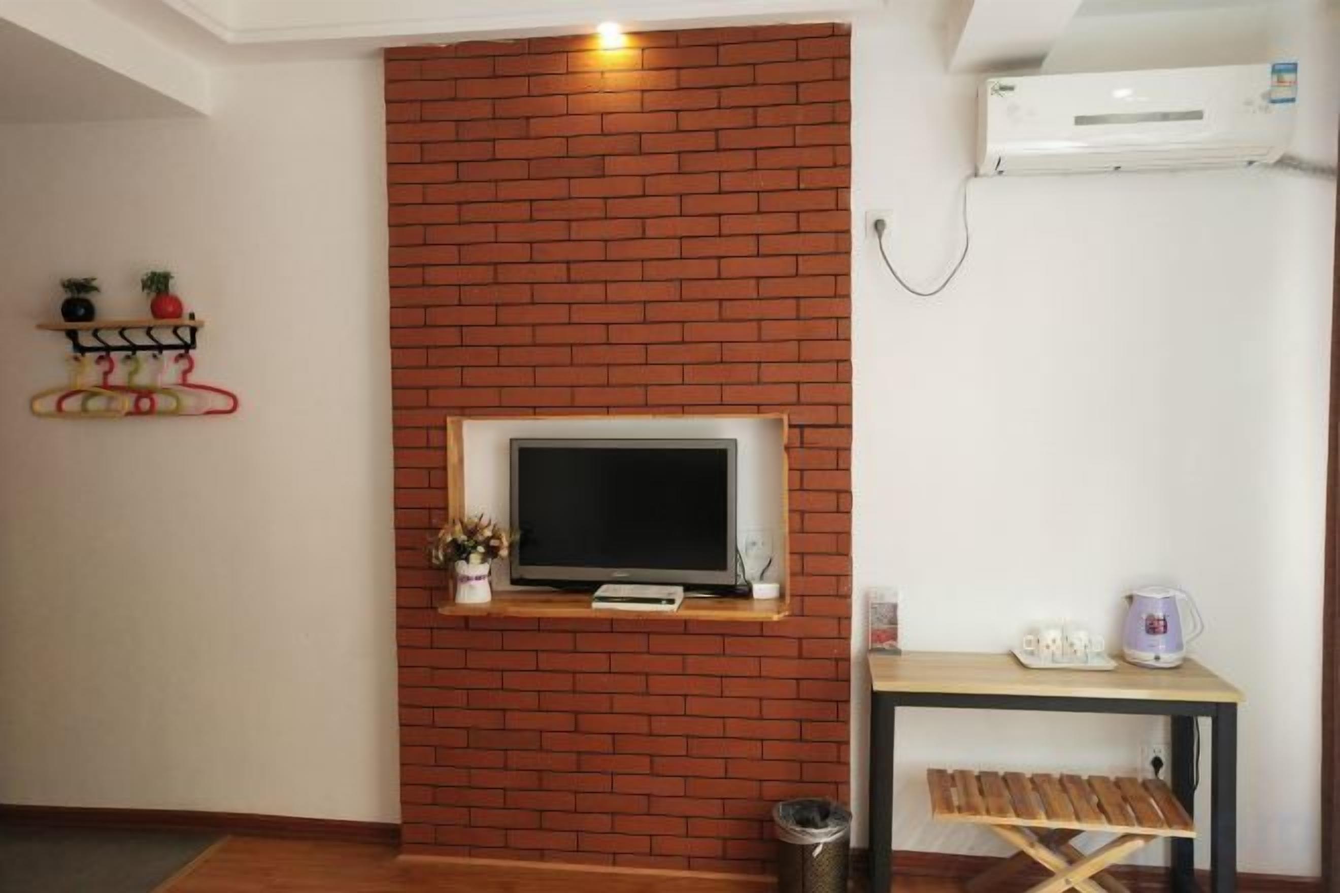 Een kamer met een bakstenen muur, een wandtelevisie, een klein tafeltje met een waterkoker en een plank met decoratieve objecten.