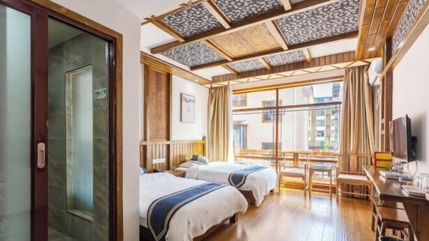 Una camera d'albergo con due letti, una scrivania in legno, una televisione e un'ampia finestra con tende.