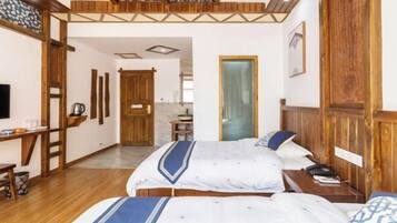 Quarto de hotel com teto de madeira, cama com colcha azul e branca, mesa de cabeceira com abajur e guarda-roupa de madeira.