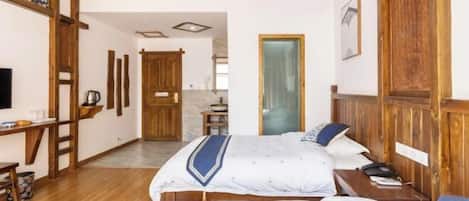 A hotel room with a wooden ceiling, a bed with a blue and white bedspread, a bedside table with a lamp, and a wooden wardrobe.