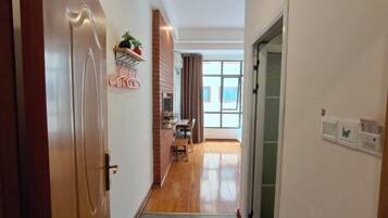 Um corredor com piso de madeira, parede de tijolos e uma janela com cortinas.