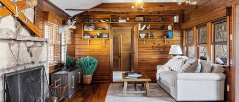 Interior acogedor de una cabaña con chimenea de piedra, estanterías de madera, un sofá y una lámpara colgante.