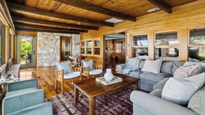 A spacious living area with wooden flooring, a stone accent wall, and a large sofa set.