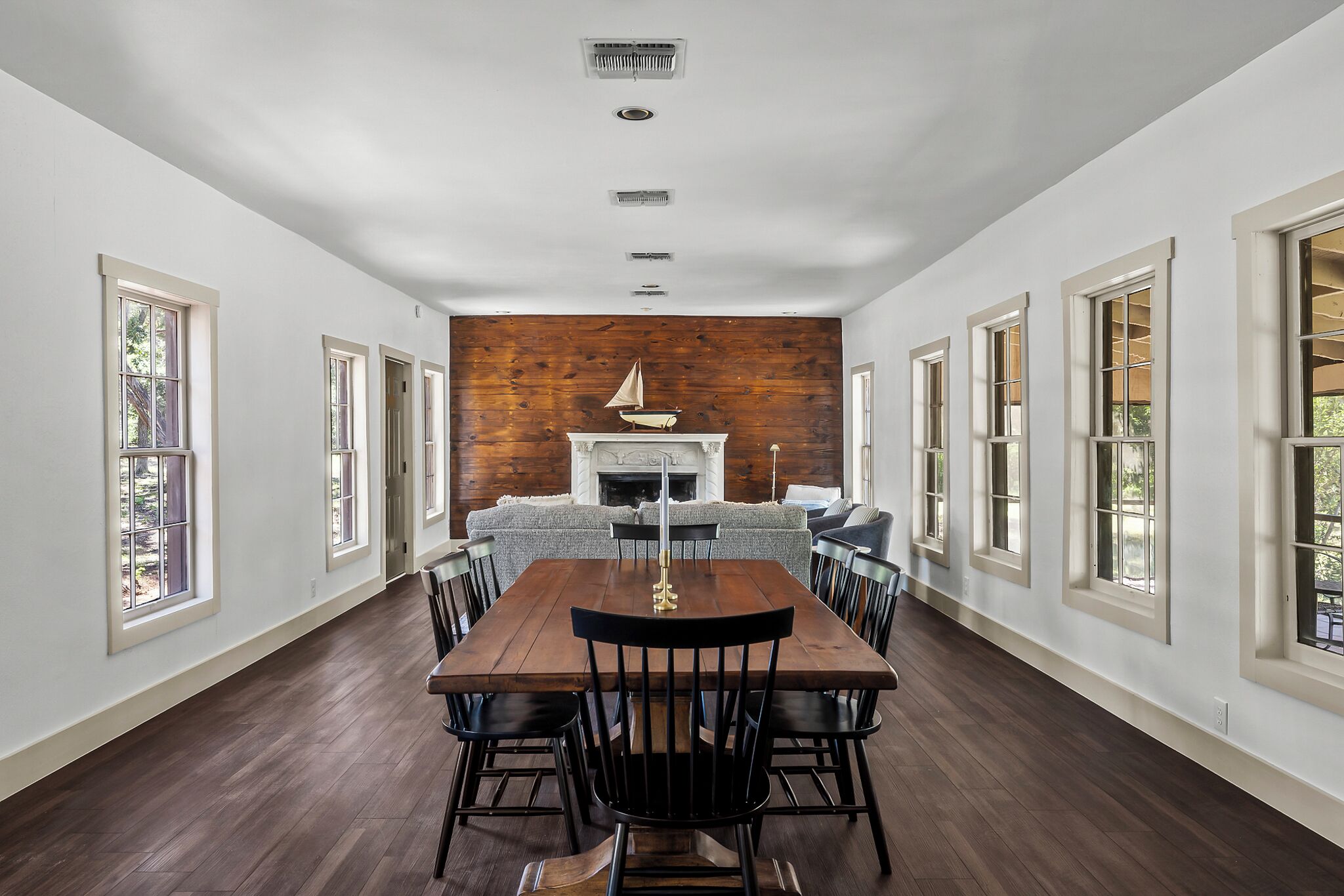 A spacious dining area with a wooden table and chairs, a fireplace, and large windows.