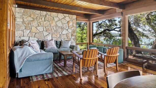 A cozy living area with a stone wall, wooden ceiling, and large windows overlooking a lake.
