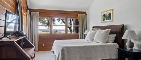Ein Schlafzimmer mit Bett, Schreibtisch, Stuhl, Lampe und einem Fenster mit Vorhängen.