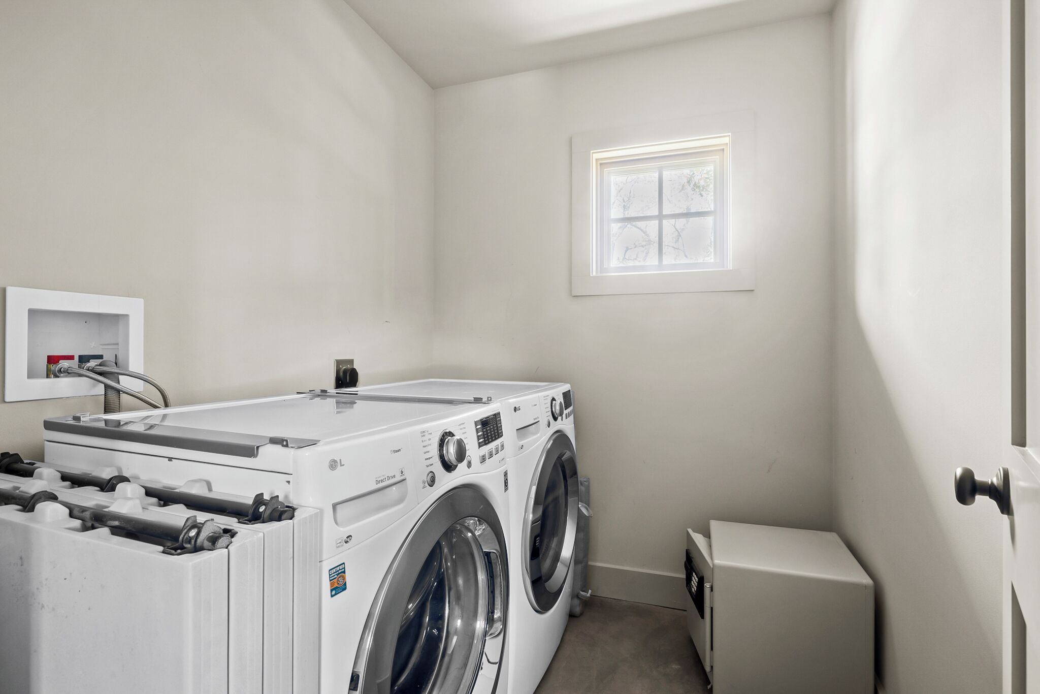 A laundry room with a front-loading washer and dryer, a small window, and a utility cabinet.
