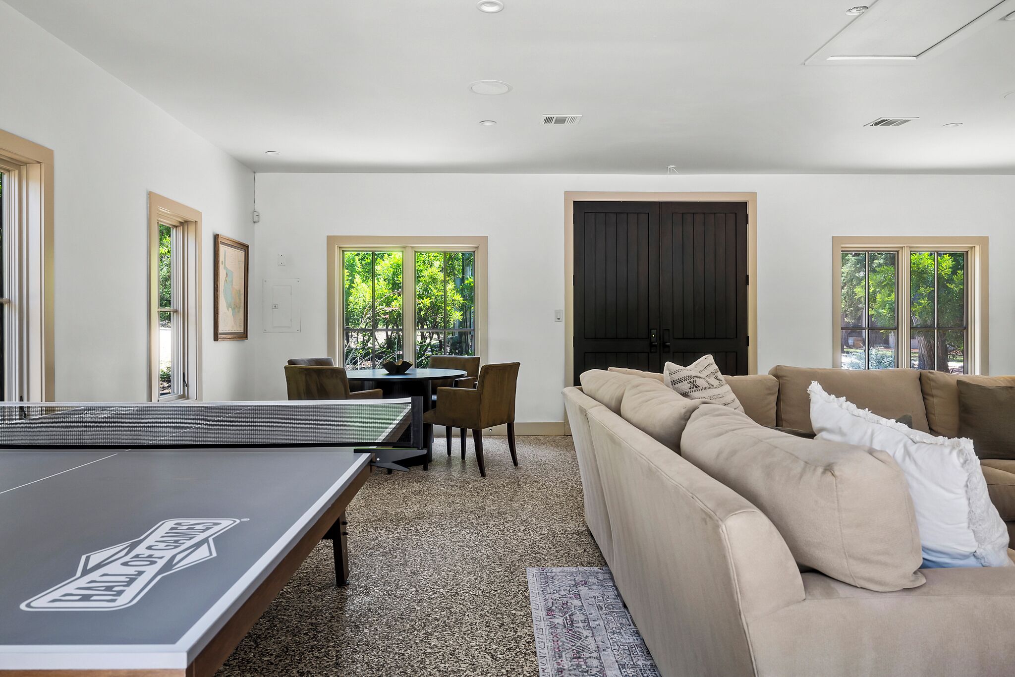 A modern living room with a ping pong table, a beige sofa, and a dining area with chairs and a table.