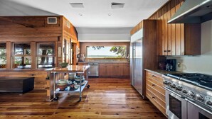 A modern kitchen with wooden cabinets, a stainless steel stove, and a large window offering a view of the outdoors.