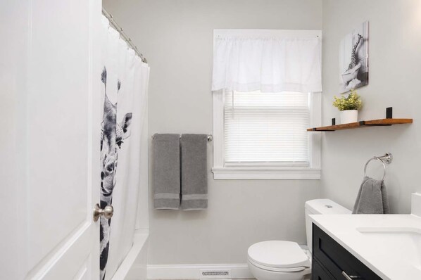 A bathroom with a shower curtain, a toilet, a window with blinds, and a towel rack.