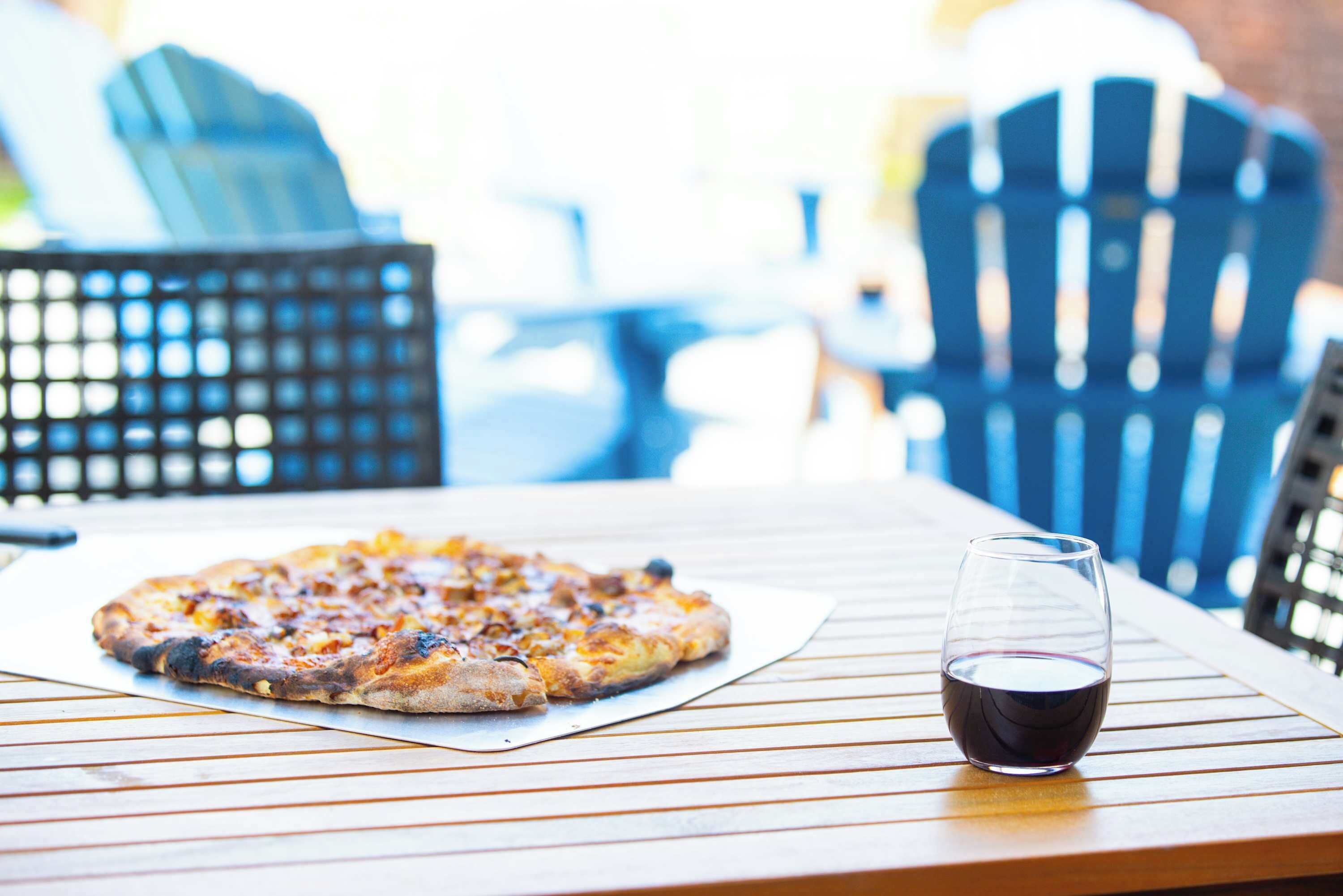 A pizza on a wooden table with a glass of red wine.