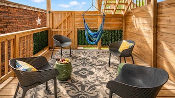 A wooden deck with two black wicker chairs, a green stool, and a hammock.