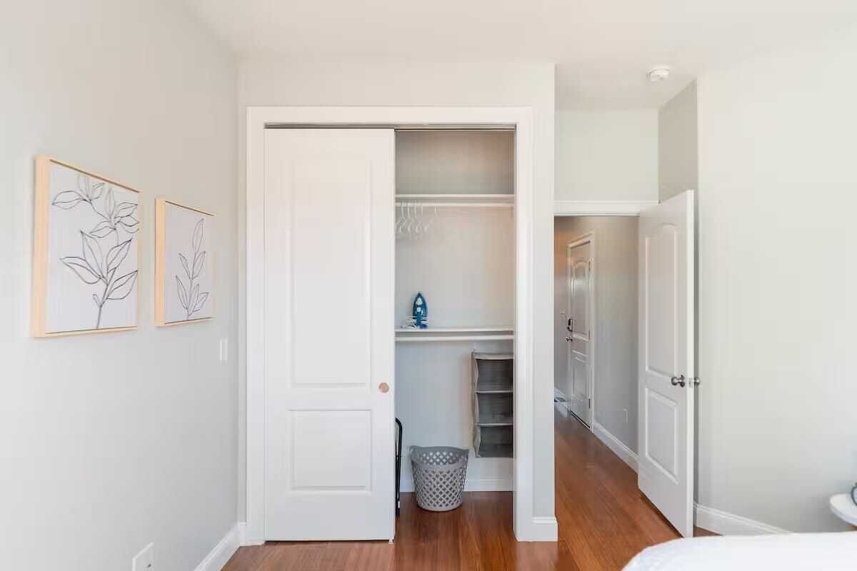 A hallway with a closet, a laundry basket, and a door leading to another room.