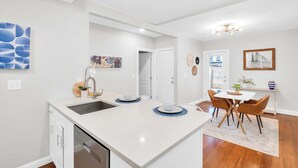 Una cocina moderna con una isla central, armarios blancos y un comedor con mesa y sillas.