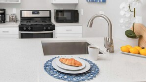 A modern kitchen with white cabinetry, stainless steel appliances, and a blue decorative placemat on the counter. - Jennifer’s Chic Modern 1st Floor Apt Private Patio (Providence)