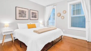 A bedroom with a bed, two bedside tables, a nightstand, a window with blinds, and wall art. - Jennifer’s Chic Modern 1st Floor Apt Private Patio (Providence)