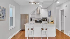 A modern kitchen with white cabinetry, stainless steel appliances, and a central island with bar stools. - Jennifer’s Chic Modern 1st Floor Apt Private Patio (Providence)