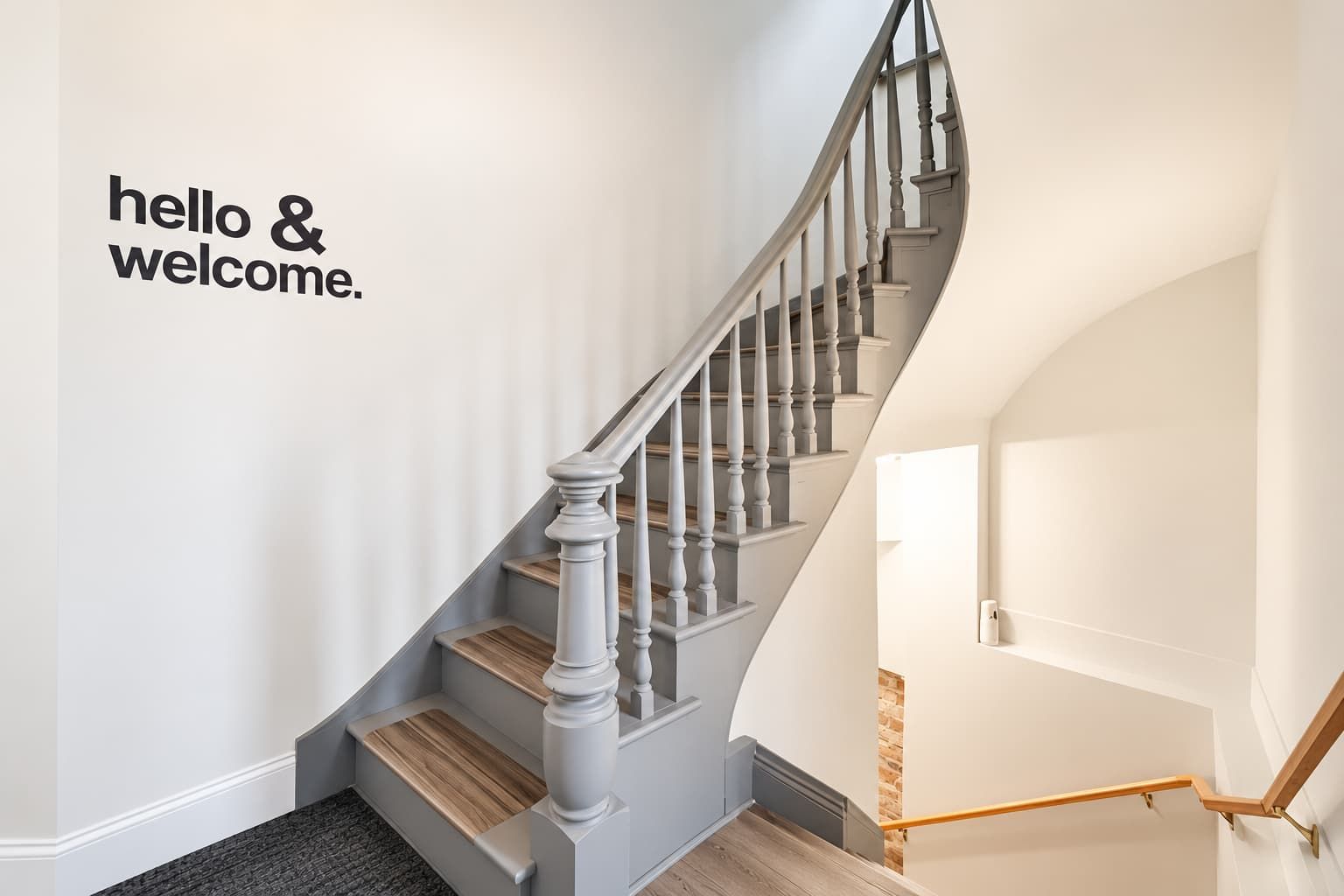 A staircase with a handrail, wooden steps, and a wall with a 'hello & welcome' sign.