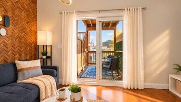 A modern living room with a sofa, coffee table, and a view of an outdoor balcony with a wooden deck and a cityscape.